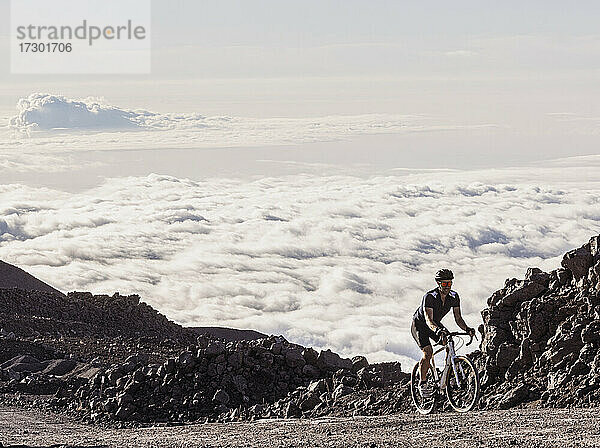 Männlicher Radfahrer fährt auf einer Schotterstraße über den Wolken auf dem Mauna Kea  Hawaii