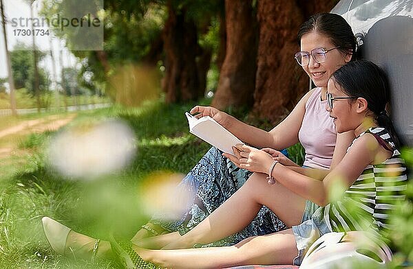 Mutter und Tochter lesen ein Buch in einem öffentlichen Park