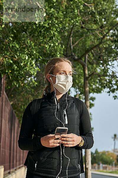 Frau in Sportkleidung und Gesichtsmaske benutzt ihr Telefon beim Gehen
