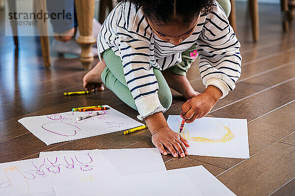 Mädchen zeichnet mit Buntstiften auf Papier zu Hause