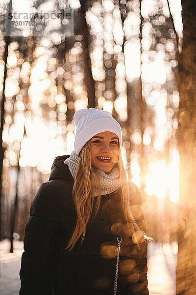 Porträt einer glücklichen jungen Frau  die im Winter inmitten von Bäumen steht