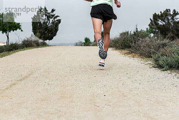 Rückansicht der Beine eines Läufers beim Training auf einem Pfad im Wald.