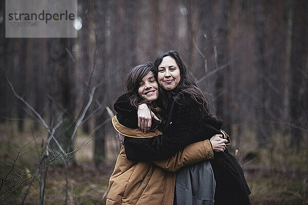 Glückliche Freundinnen umarmen sich und lächeln im Freien im Wald in Deutschland