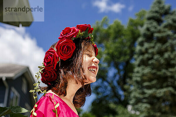 Ein lachendes kleines Mädchen mit geschlossenen Augen trägt eine Krone aus Rosen