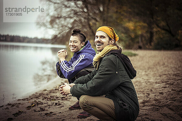 zwei glückliche  schräge Freunde sitzen im Winter am See und lachen und plaudern