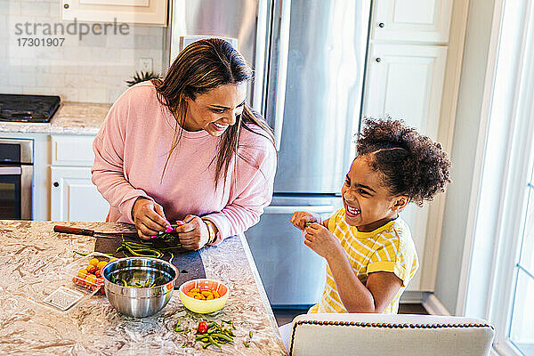 Lächelnde Tochter hilft Mutter bei der Zubereitung von Essen in der Küche zu Hause