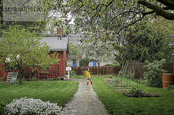 Ein kleines Mädchen spielt im strömenden Regen im Hinterhofgarten