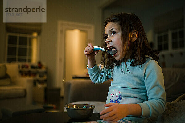 Mädchen isst Müsli vor dem Fernseher in den frühen Morgenstunden