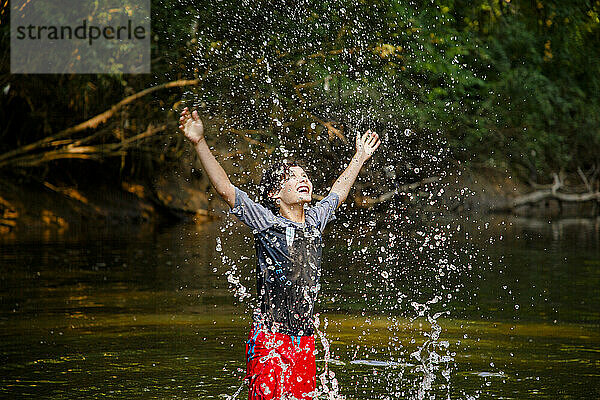 Ein fröhlicher Junge spielt im Fluss und schleudert Wassertropfen hoch in die Luft