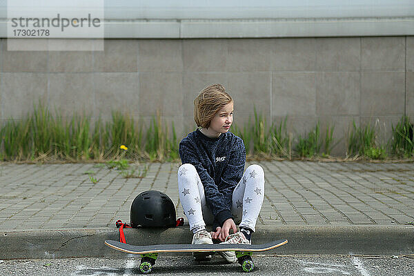 Das Mädchen setzt sich neben das Skateboard.