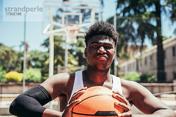 Porträt eines wütenden schwarzen Afro-Jungen mit trotzigem Blick  der den Basketball mit seinen Händen zusammendrückt. Bereit  ein Spiel zu spielen.