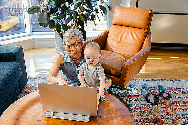 Ältere Frau sitzt mit ihrer Enkelin und führt einen Videogespräch auf dem Laptop
