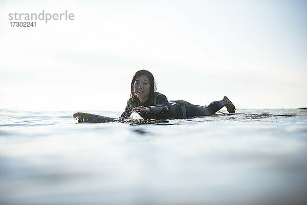 Asiatische Frau paddelt bei Sonnenaufgang nach Wellen und surft im Sommer
