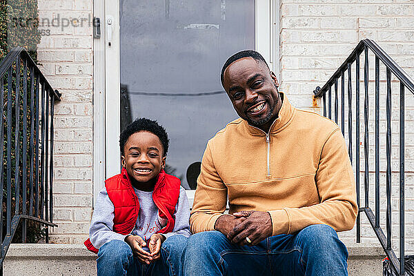 Porträt eines glücklichen Vaters und eines Sohnes  die am Eingang eines Hauses sitzen