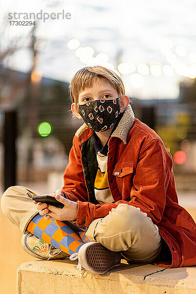 Teenager mit Telefon in der Hand und Maske während der globalen Pandemie