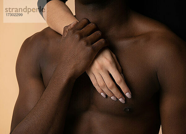 Nackte Brust eines afroamerikanischen Mannes  der die Hand einer Frau im Studio hält