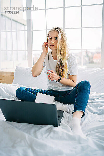 Blondes Mädchen arbeitet am Laptop im Bett