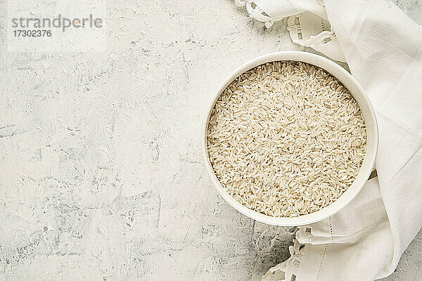 Draufsicht auf eine mit rohem weißem Reis gefüllte Schale auf einem strukturierten Hintergrund