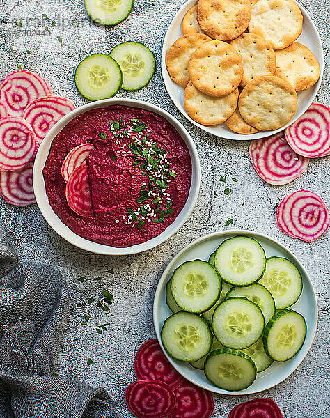 Schale mit Rüben-Hummus  Gemüse und Crackern auf grauem Hintergrund.