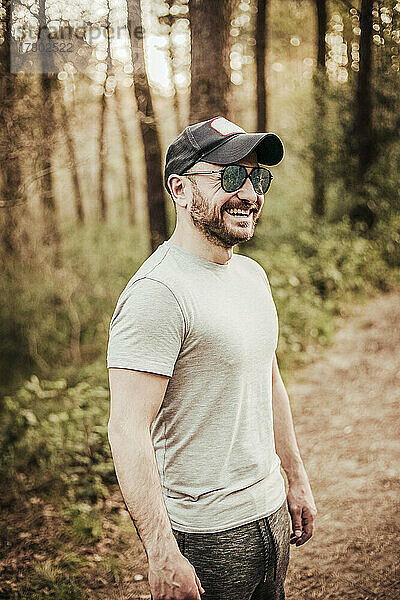 Mann mit Mütze und Sonnenbrille lächelnd in einem schönen Wald