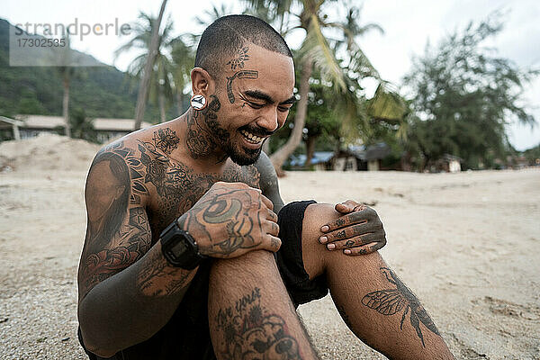 hipster kerl mit tätowierung sitzt am strand in thailand