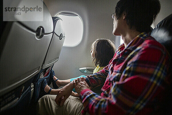 Ein kleines Mädchen und sein Vater sitzen zusammen im Flugzeug und schauen aus dem Fenster