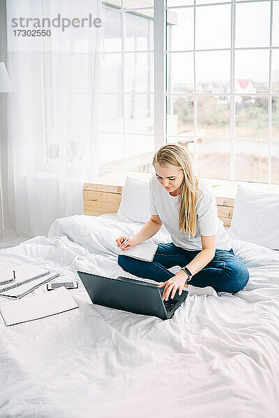 Blondes Mädchen arbeitet am Laptop im Bett