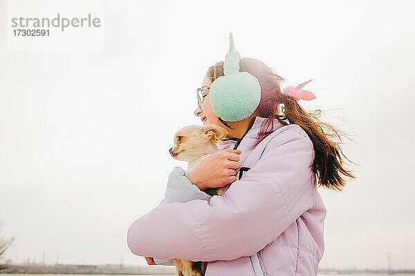 Porträt eines glücklichen Teenager-Mädchens mit ihrem kleinen Chihuahua-Hund. Ein Mädchen auf dem Hintergrund der Natur umarmt ihren Chihuahua-Hund in der Kleidung.