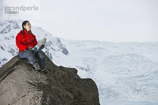 Wanderin beim Kartenlesen auf einem Felsen oberhalb des Gletschers