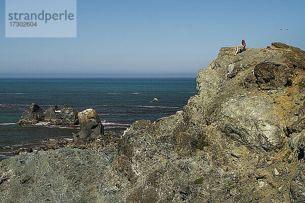 Frau in einem grünen Kleid sitzt auf der Oregon Coast Cliff