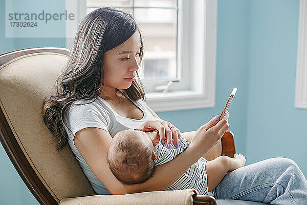 Asiatische Mutter hält ihren neugeborenen Sohn im Arm und kauft Lebensmittel online im Internet.