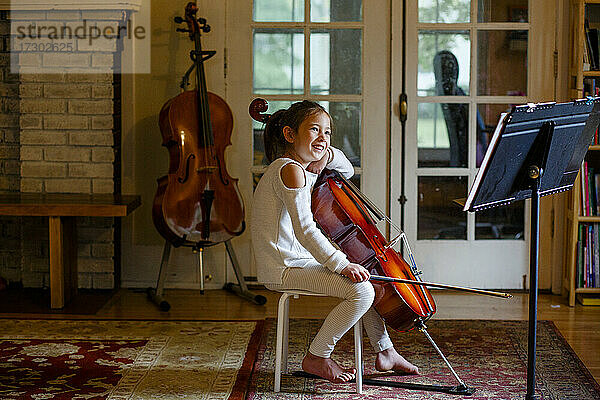 Ein glückliches barfuß gehendes Mädchen übt im Wohnzimmer Cello