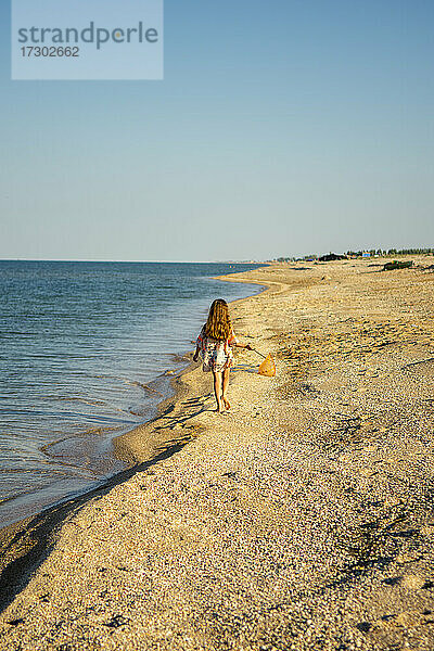 Ein Mädchen geht bei Sonnenuntergang am Meer entlang