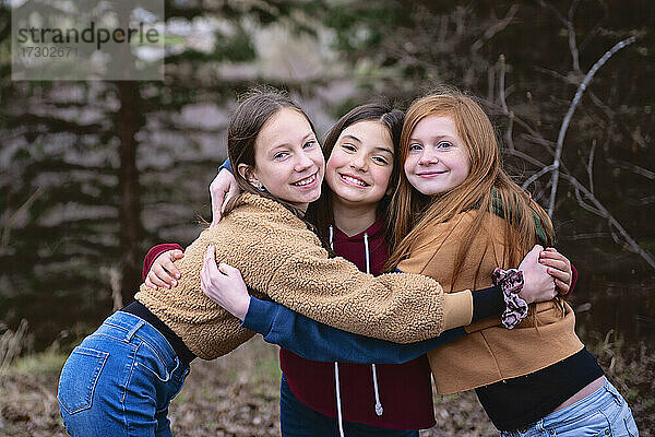Drei Mädchen im Teenageralter stehen im Freien und umarmen sich gegenseitig.