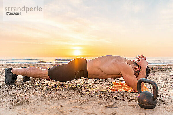 muskulöser hispanischer Mann macht Planke am Strand bei Sonnenaufgang