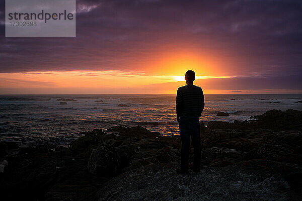 Mann beobachtet einen schönen Sonnenuntergang Felsen Strand friedliche Landschaft