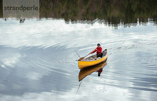 Ein Jugendlicher paddelt allein mit einem Kanu auf einem ruhigen See in Kanada.
