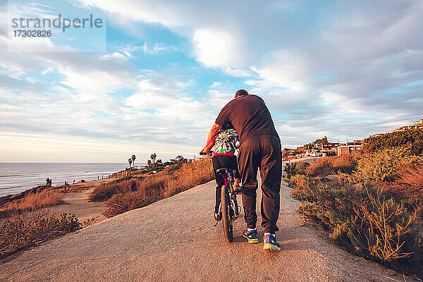 Vater hilft seinem Sohn beim Radfahren auf einem Küstenweg.