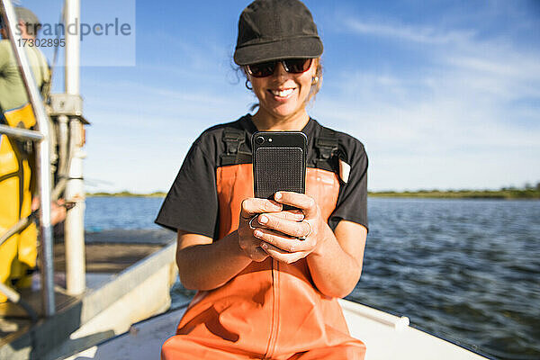Frau mit Telefon bei der Arbeit auf dem Wasser in einer Aquakultur-Austernzucht