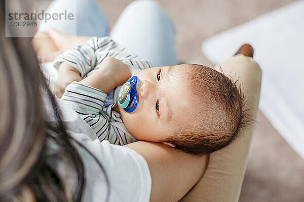 Zwei Monate Baby liegend mit Schnuller im Mund auf den Armen der Mutter.
