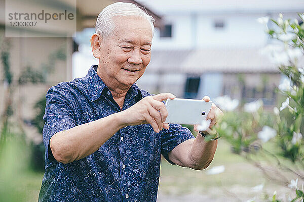 Glücklicher asiatischer älterer Mann  der ein Foto mit seinem Mobiltelefon macht.