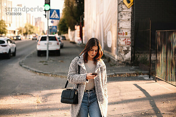 Nicht-binäre Frau benutzt Smartphone beim Spaziergang in der Stadt