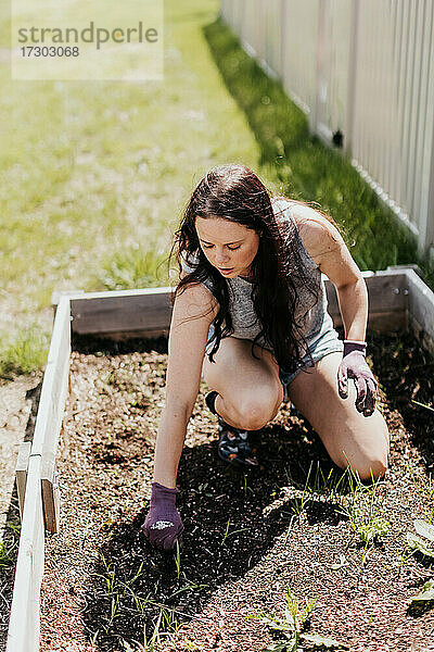 Frau räumt an einem sonnigen Sommertag das Gartenbeet im Hinterhof auf