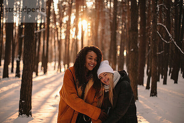 Porträt von glücklichen Freundinnen  die sich in einem verschneiten Park umarmen