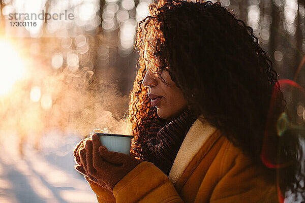 Junge Frau mit einer Tasse heißem Tee im Freien stehend im Winter