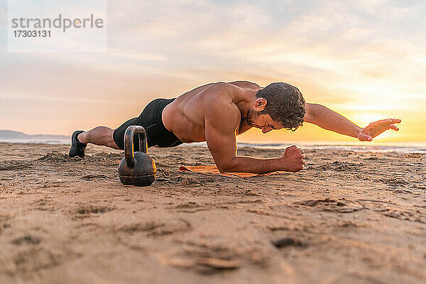 muskulöser hispanischer Mann macht Planke am Strand bei Sonnenaufgang