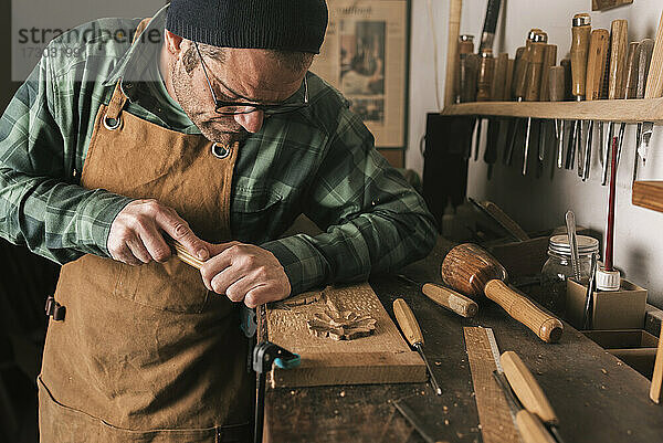 Seitenaufnahme eines Tischlers bei der Arbeit an einer Holzschnitzerei mit einem Meißel.