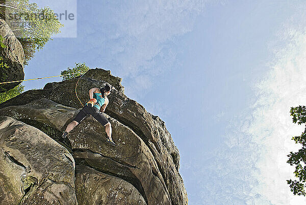 Frau klettert auf den Sandsteinfelsen am Harrison's Rock in England