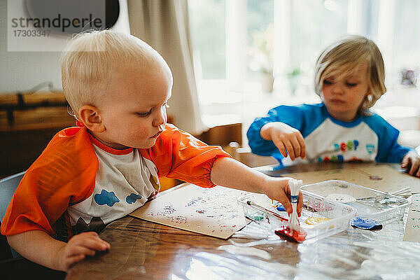 Blonde kleine Kinder malen mit vielen bunten Farben zu Hause