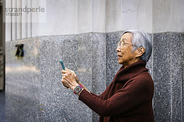 Seitenansicht einer älteren Frau  die ein Smartphone benutzt  während sie an der Wand steht